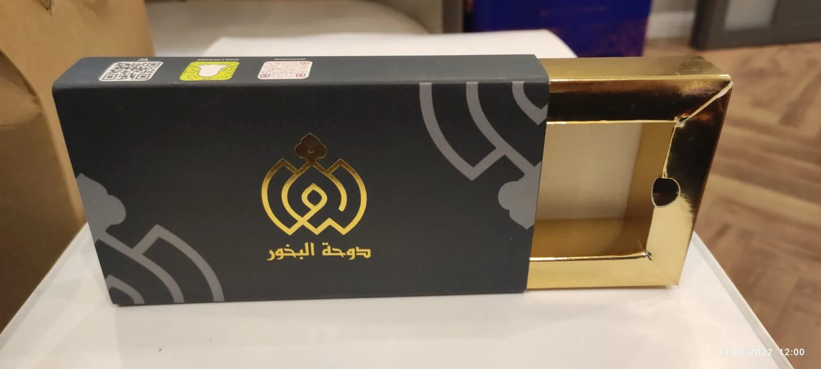علبة درج منزلقة مطبوعة بالأسود مع شعار مذهّب وصينية داخلية ذهبية، والدرج مسحوب جزئياً